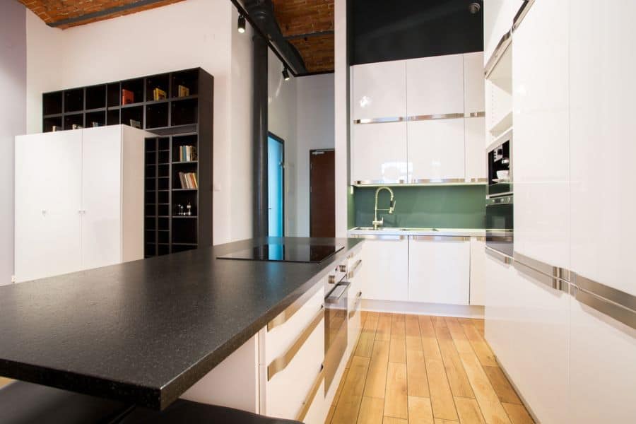 Modern kitchen with white cabinets, black countertop, and green backsplash.