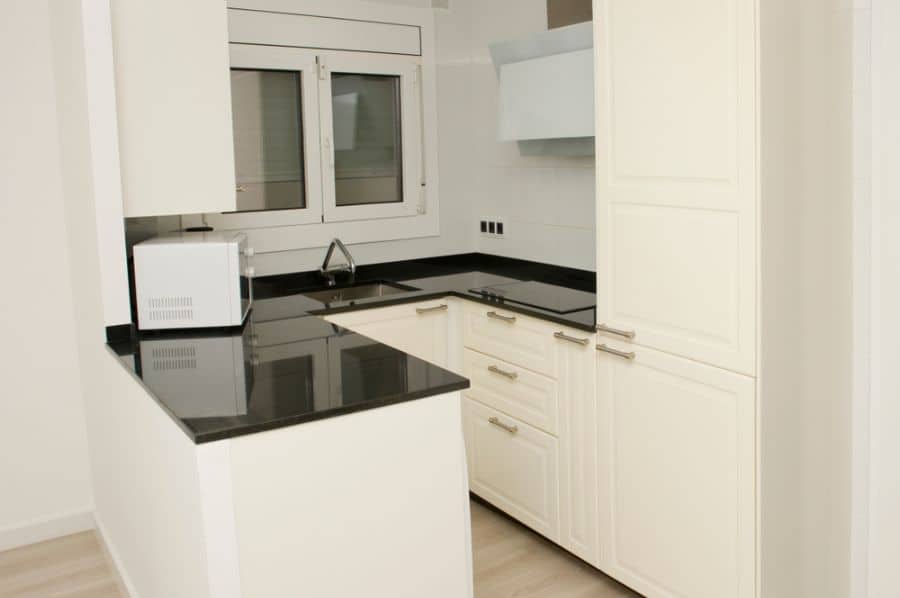Compact kitchen with white cabinets and black countertops.
