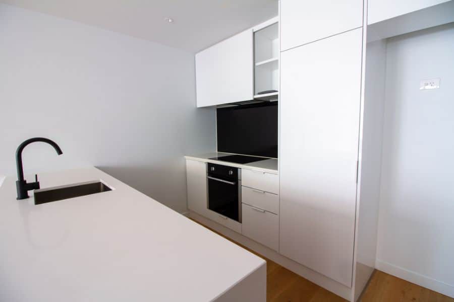 Minimalist kitchen with white cabinets, black backsplash, and black faucet.