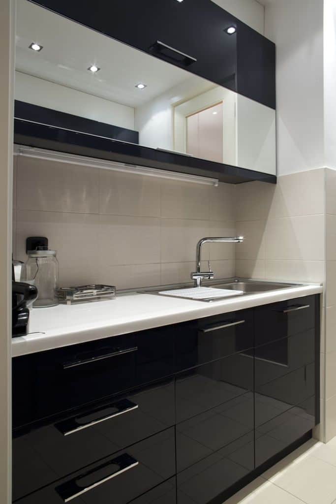 Compact kitchen with black glossy cabinets, white countertop, and stainless steel sink.