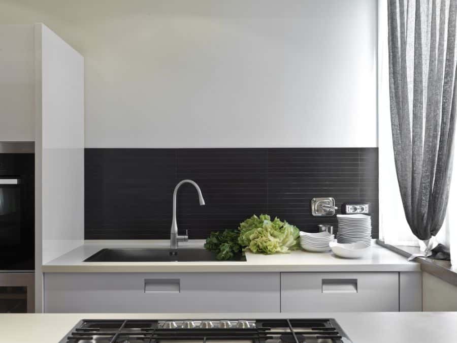 Modern kitchen with black backsplash, white cabinets, and stainless steel sink.