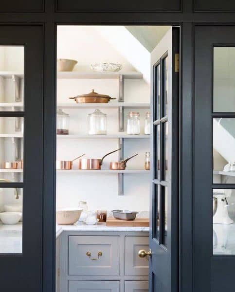Small pantry with glass doors, copper cookware, and neatly arranged shelves.