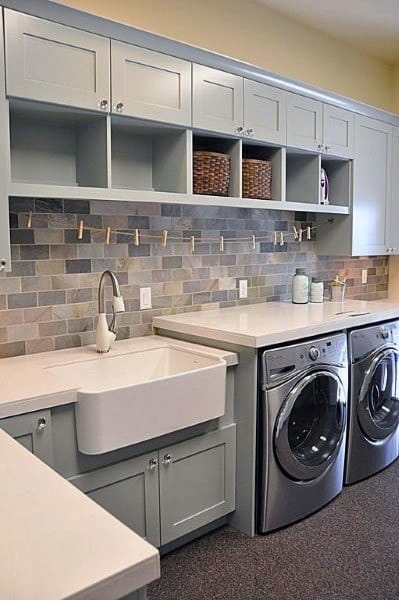 Laundry room featuring pastel cabinets, a farmhouse sink, and a colorful tiled backsplash with hanging pegs.