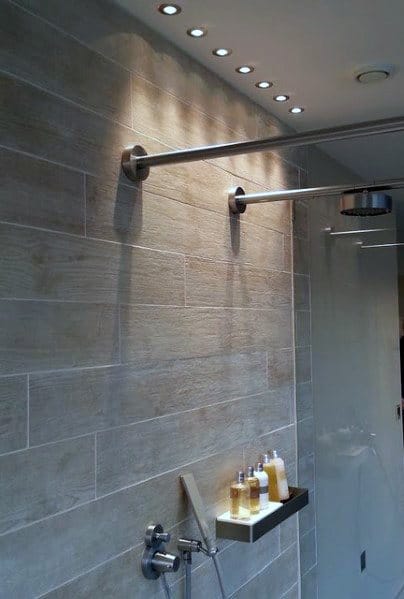 Modern shower with sleek, light gray tiles, overhead small LED lights providing focused illumination and a minimalist shelf for toiletries