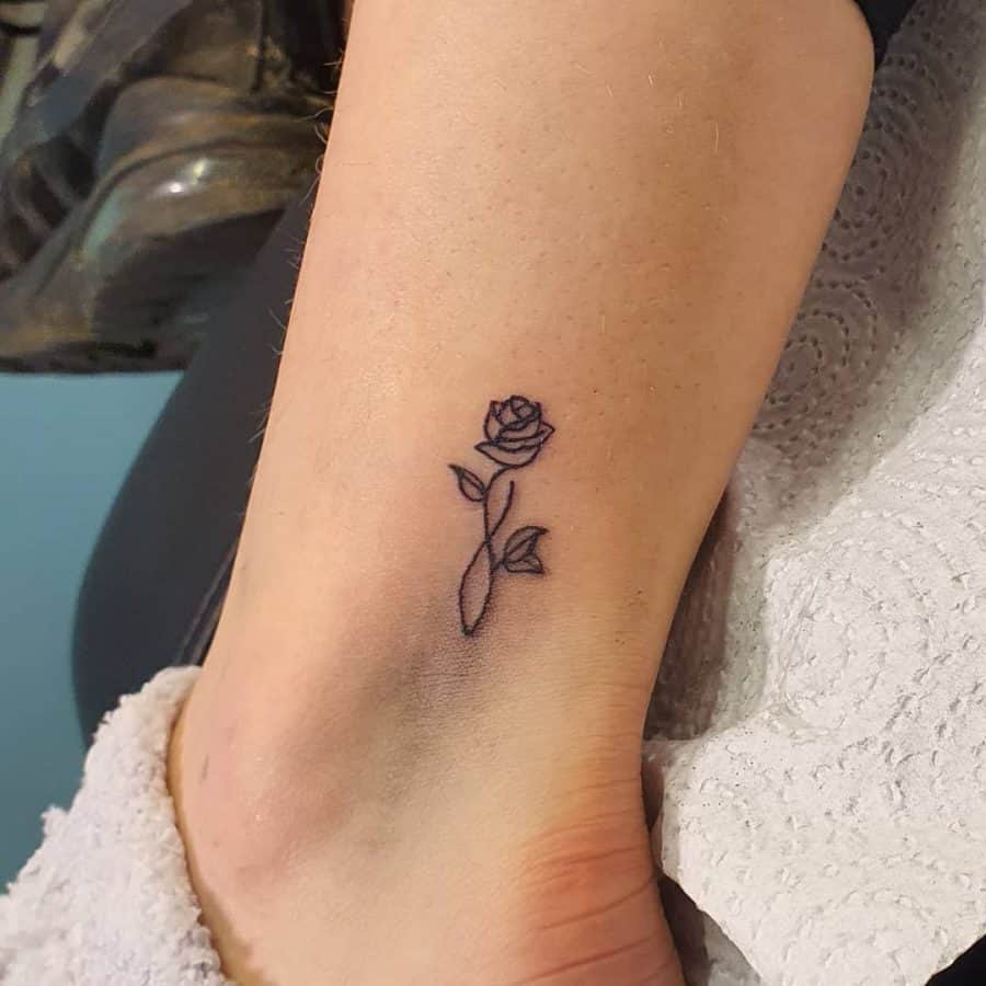 A simple and elegant tattoo of a single rose with a delicate stem and leaves, capturing timeless beauty.