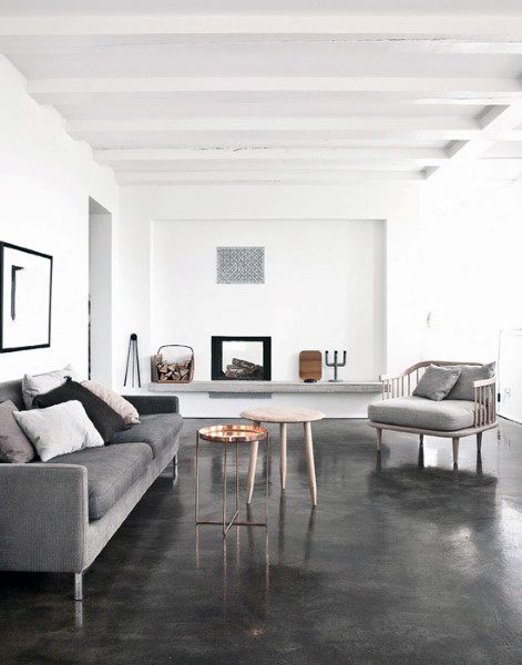 Minimalist living room with a gray sofa, armchair, small tables, and a fireplace on sleek concrete floors