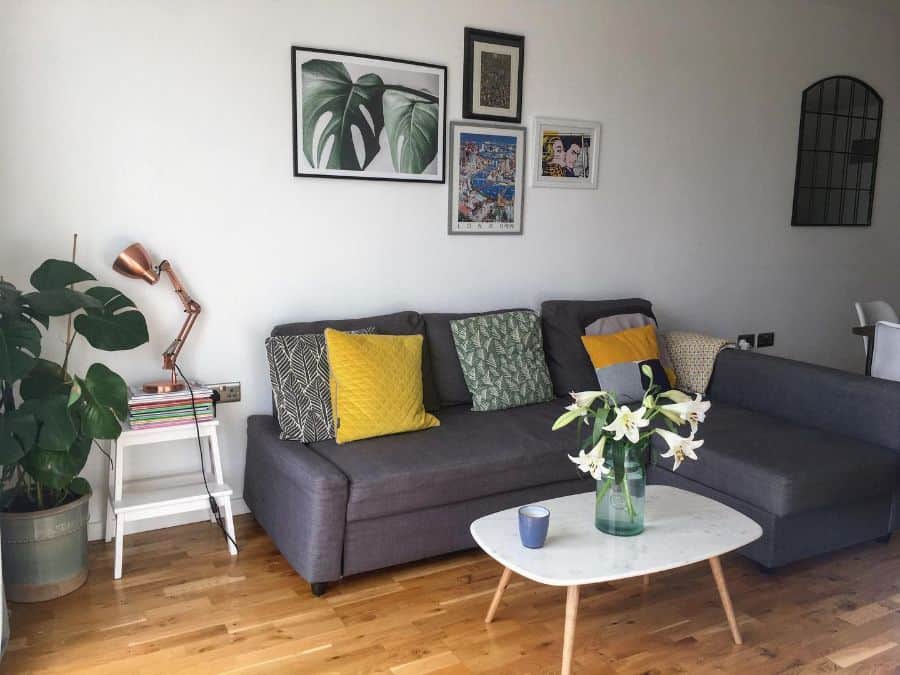Cozy living room with a gray sofa, colorful cushions, a small white coffee table with flowers, and framed wall art