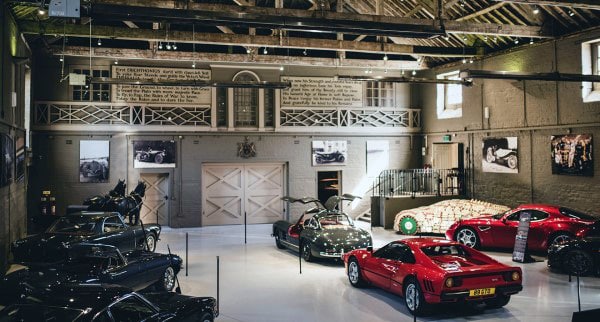 A garage room with vintage cars displayed, featuring red and black models, under wooden beams with framed photos