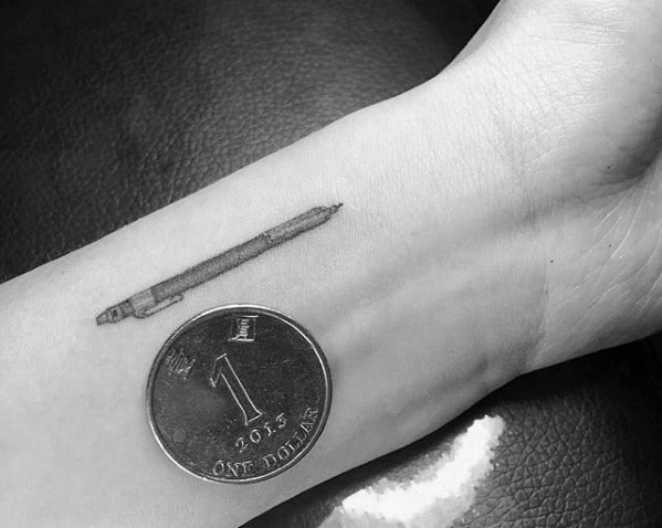 A sleek tattoo of a pencil graces the arm, perfectly complemented by a one-dollar coin placed next to it for scale