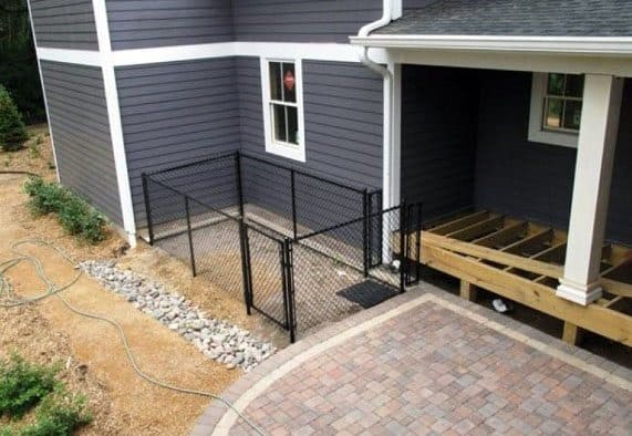 Black chain-link fence surrounds a house with gray siding, brick patio, and wooden deck