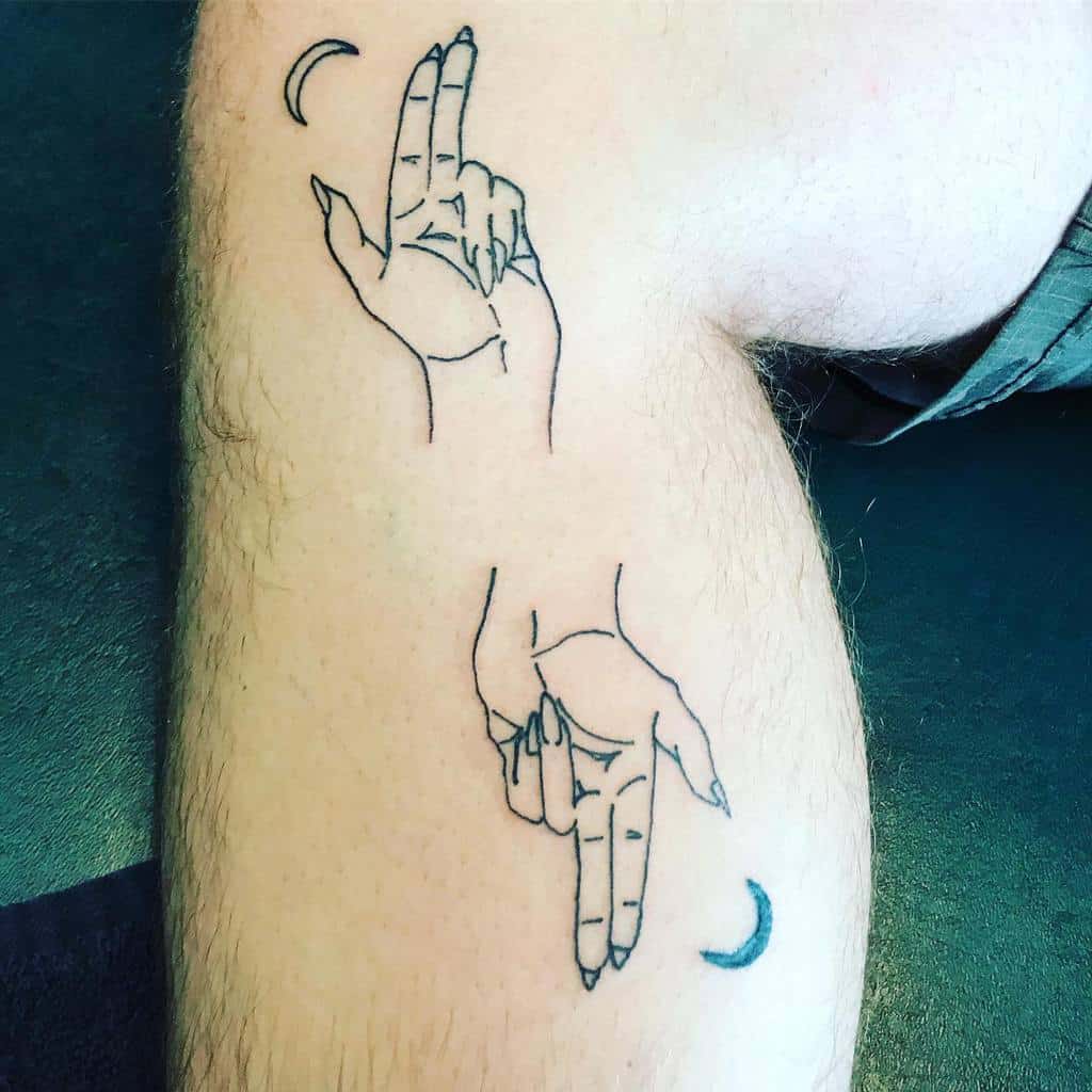 Minimalist tattoo showcasing two hands pointing in opposite directions, paired with crescent moons for a simple and celestial design