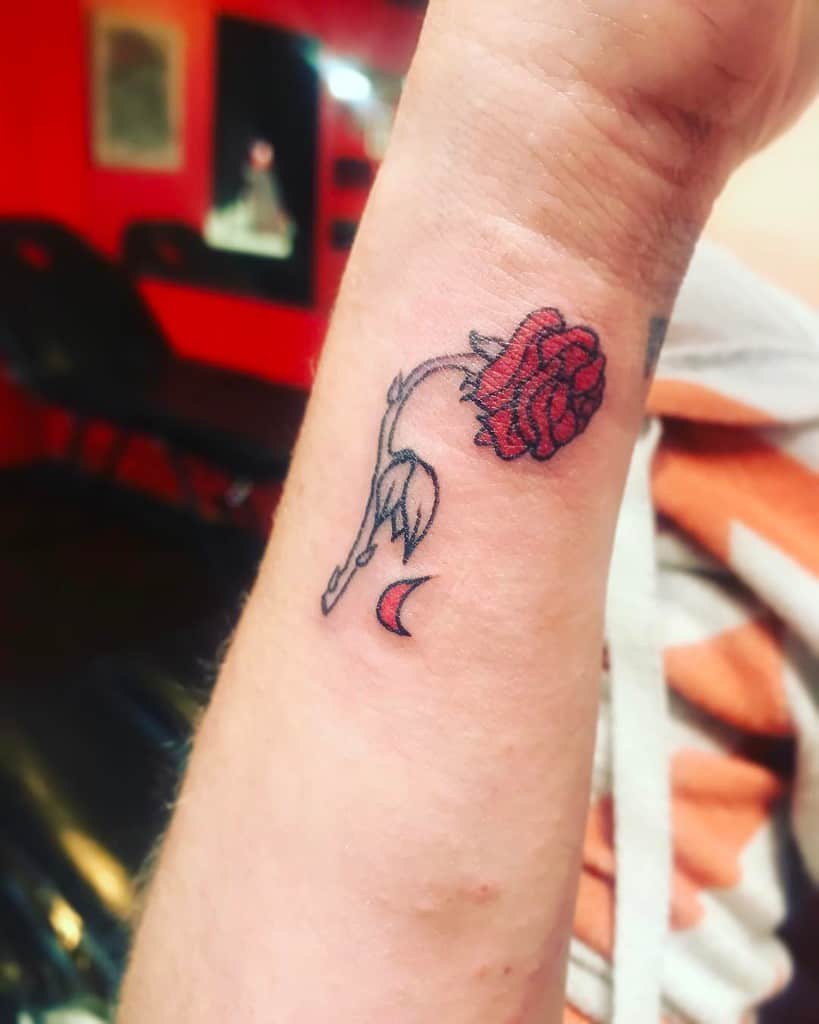 A small and minimalist Beauty and the Beast rose tattoo with a simple red rose and delicate linework, accompanied by a crescent moon