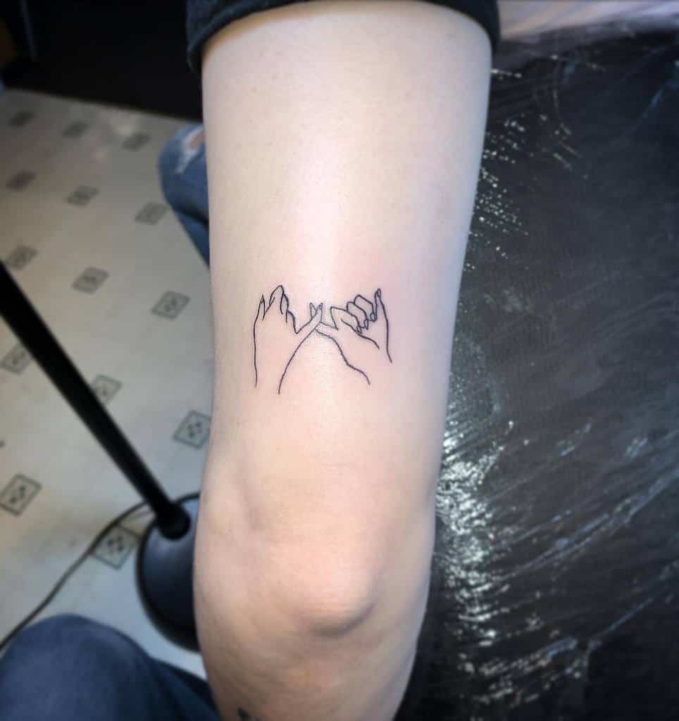 Tattoo on an arm depicting two hands making a pinky swear gesture