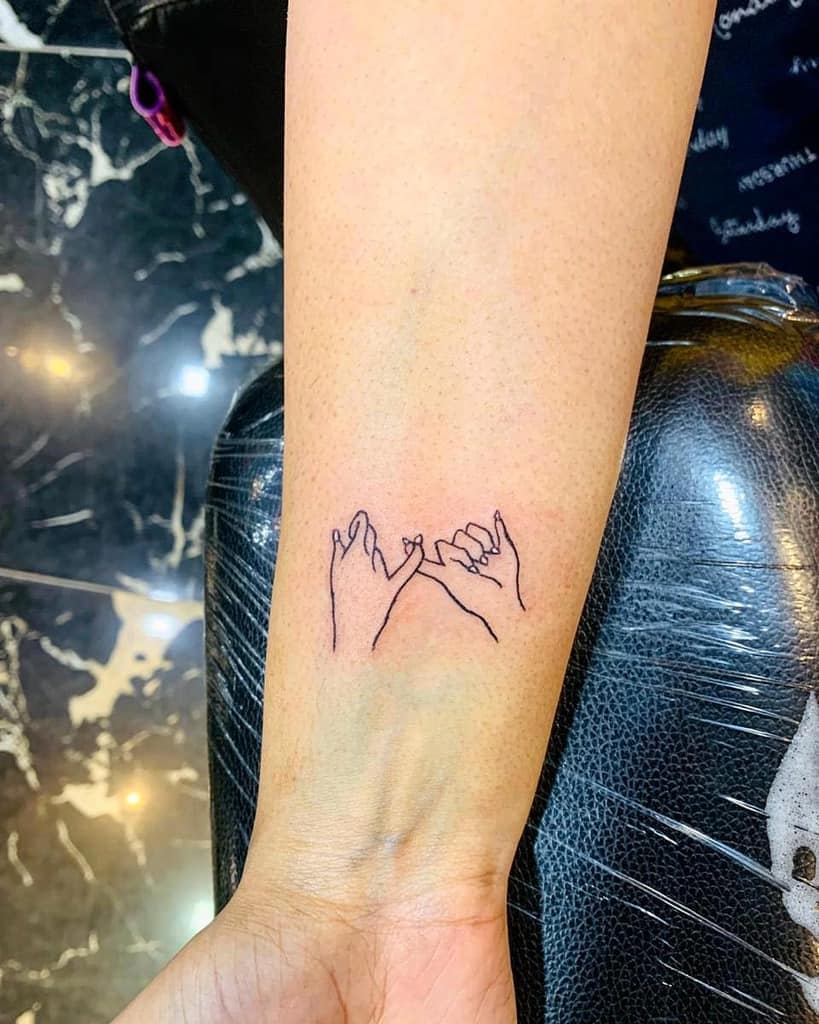 Minimalist tattoo of two hands making a pinky promise, located on a wrist