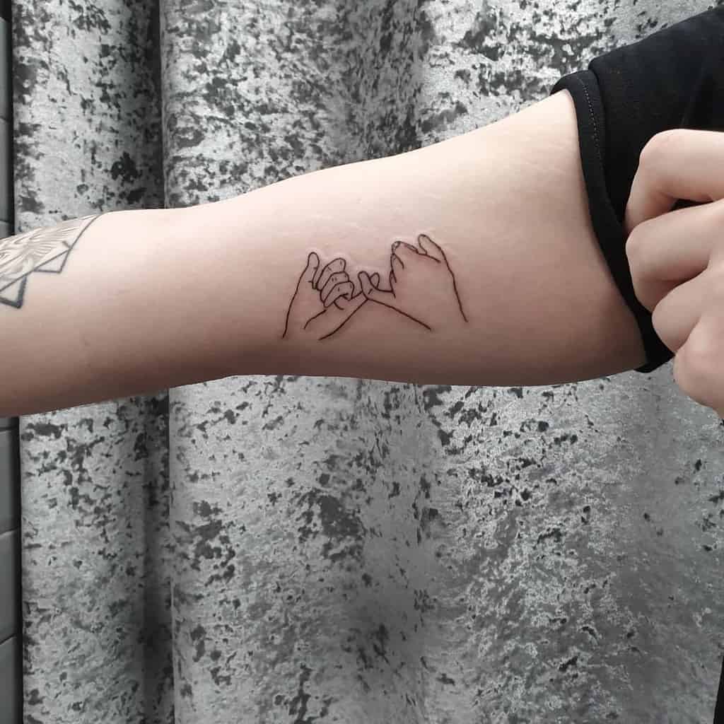 Arm tattoo of two hands making a pinky promise