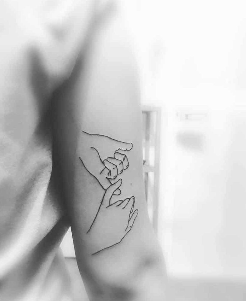 Minimalist pinky promise tattoo with clean line art, placed on the back of the upper arm, shown in a black and white photo
