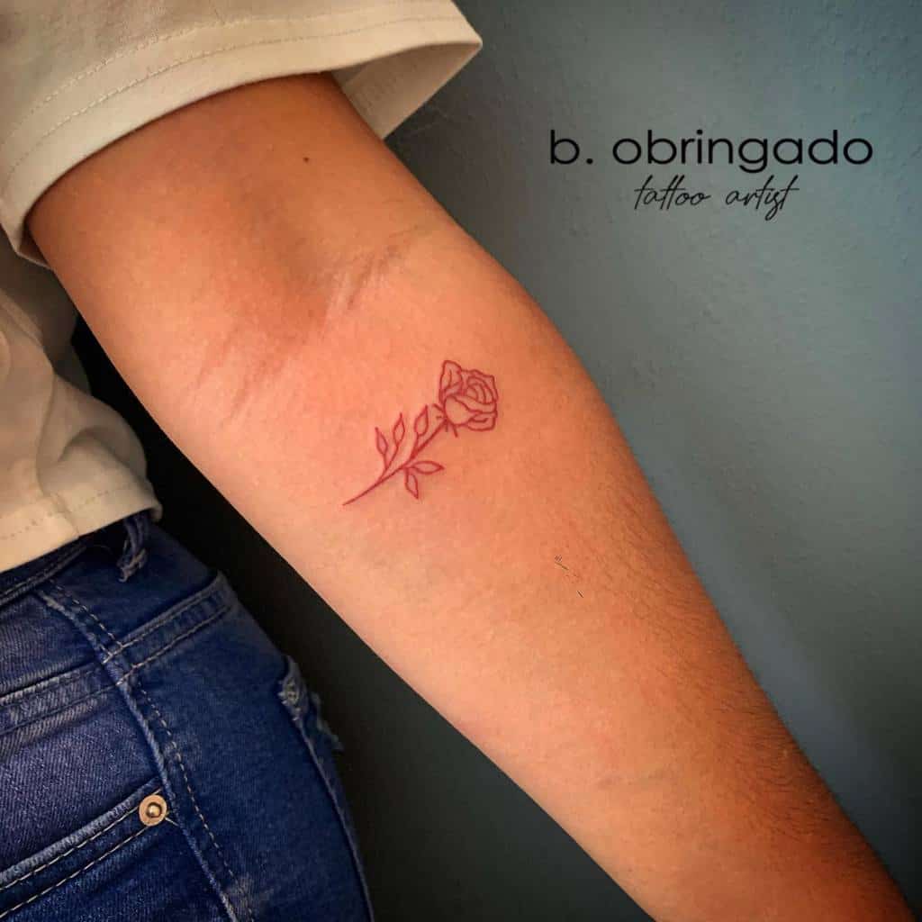 A striking minimalist red rose tattoo graces the forearm, capturing elegance in its simplicity