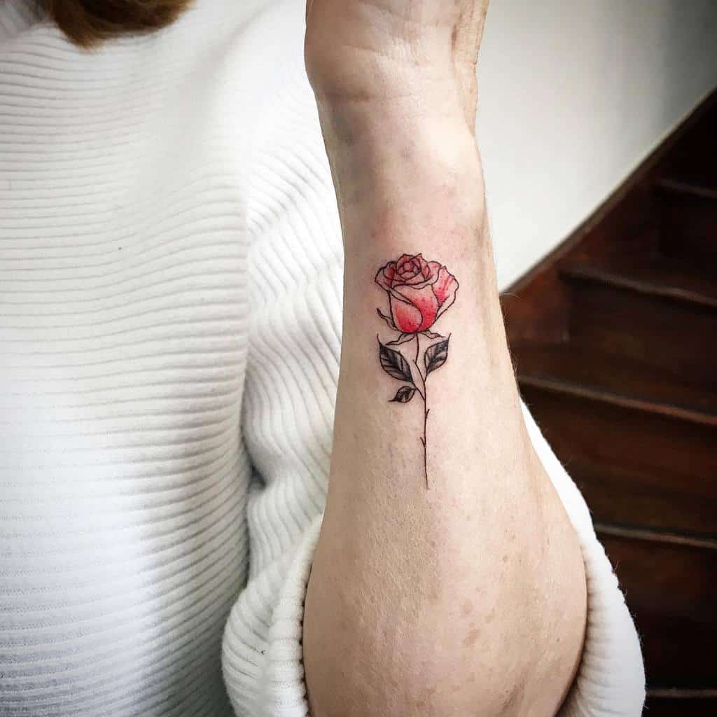 A small red rose tattoo adorns a person's forearm, adding a touch of elegance and color