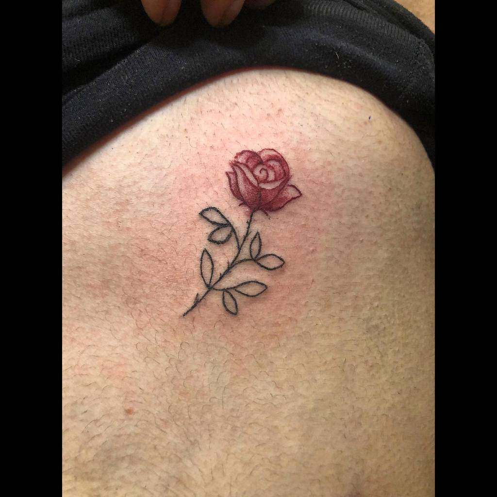 A delicate tattoo features a small red rose adorned with lush green leaves, flourishing elegantly on the skin