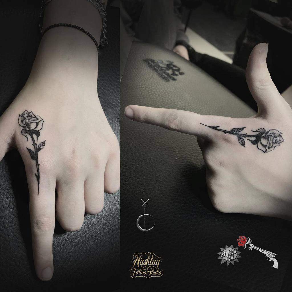 A small minimalist rose tattoo on the hand, with a single stem and delicate shading, positioned on the side of the finger and hand