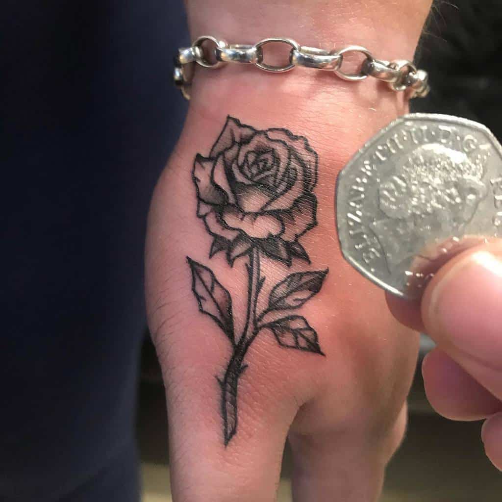 A small minimalist rose tattoo on the hand, outlined in black with detailed shading