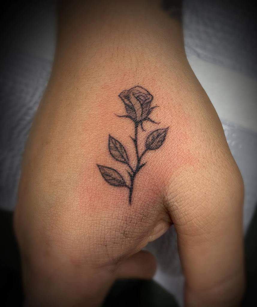 A delicate hand adorned with a small black ink rose tattoo graces the hand, adding an understated elegance