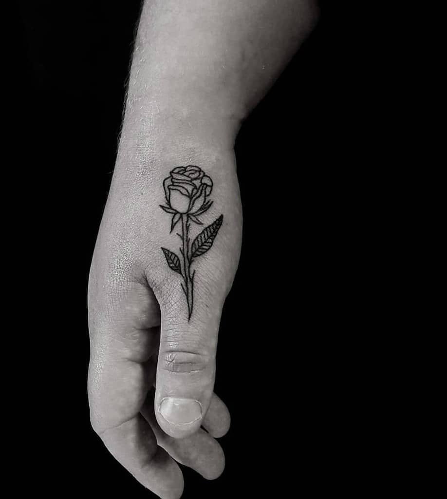 A delicate black ink rose tattoo blooms elegantly across the back of a hand