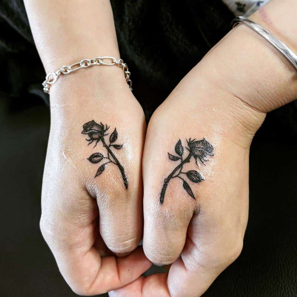 Hands elegantly adorned with matching black tattoos that beautifully depict roses on the thumbs