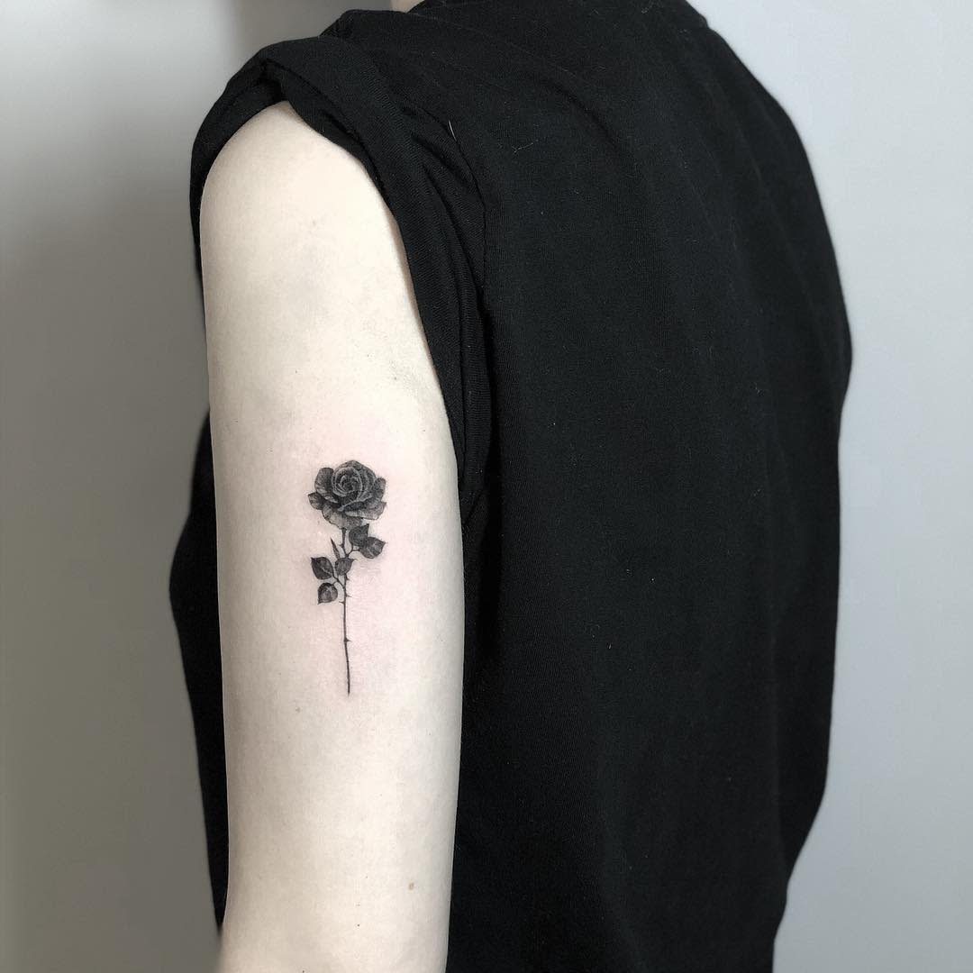 Minimalist arm tattoo of a single black rose with a slender stem and small leaves, exuding simplicity and grace