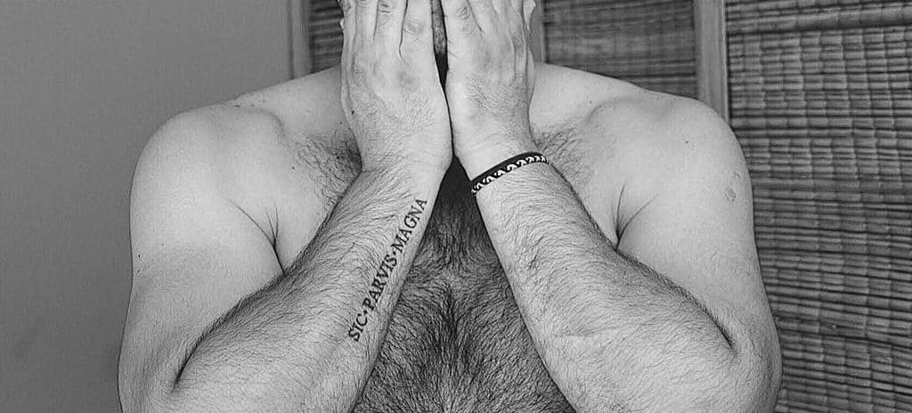 Minimalist forearm tattoo of 'Sic Parvis Magna' in bold black script, showcased in a black-and-white portrait