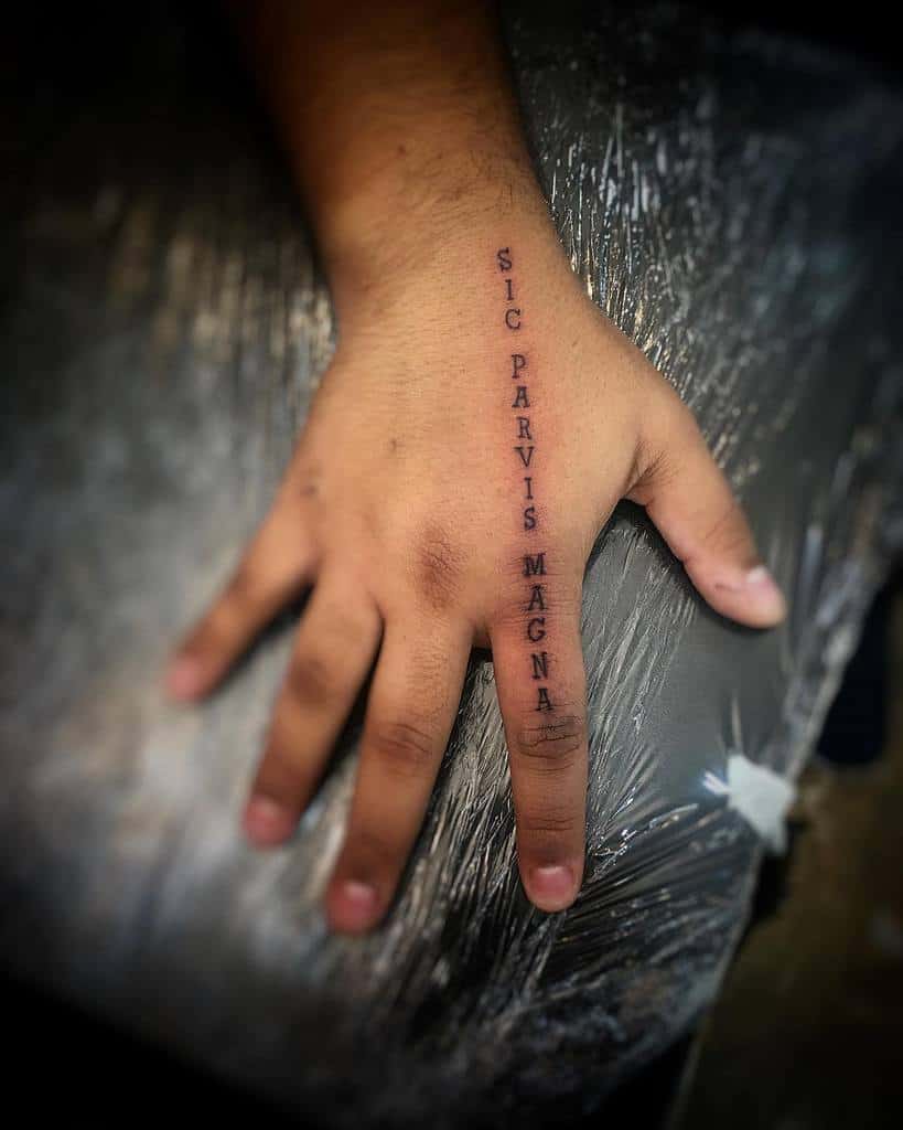 A hand with the tattoo "Sic Parvis Magna" on the side of the pinky finger
