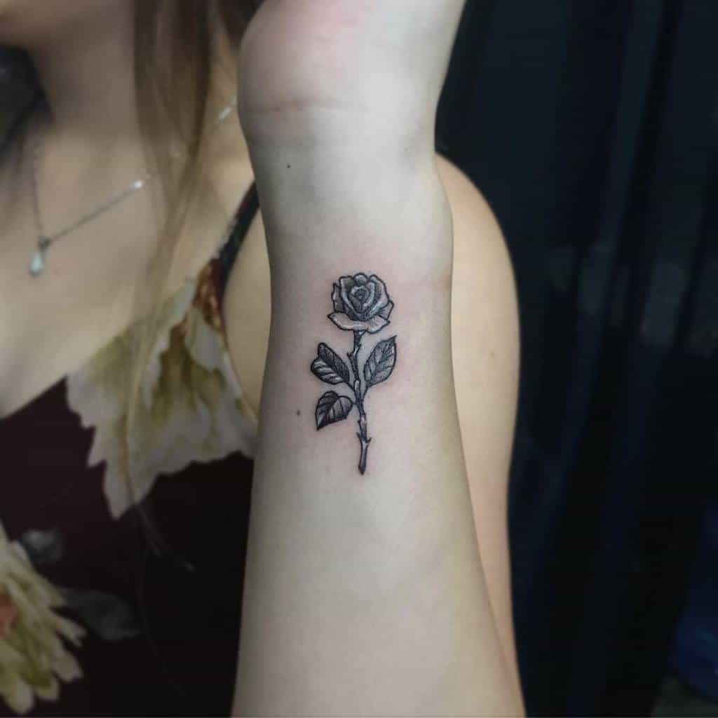 Minimalist black rose tattoo on a woman's forearm