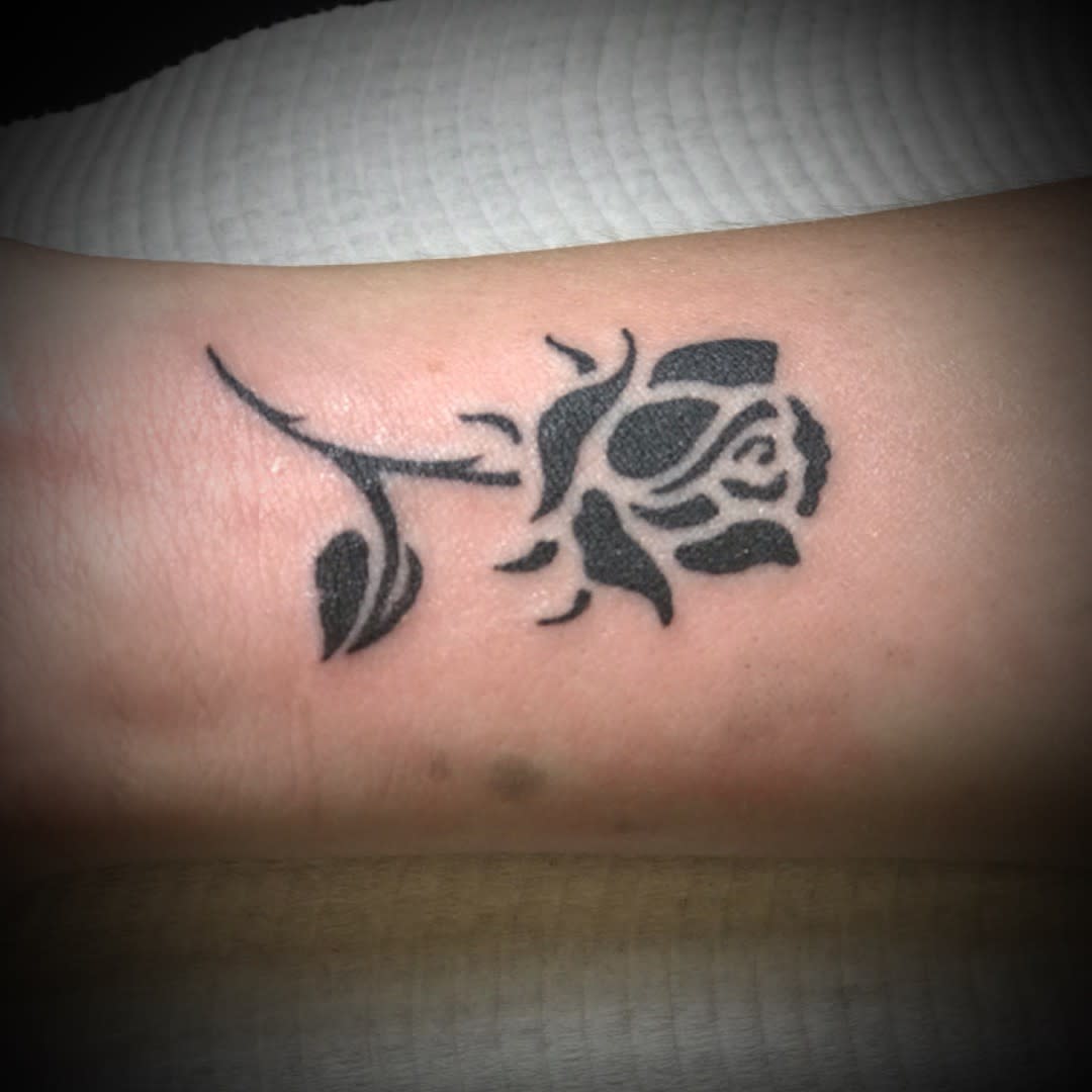 Black rose tattoo with stem and leaf on skin background