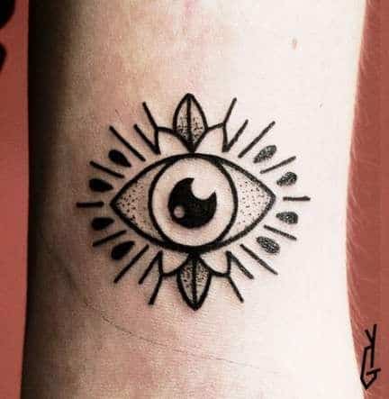 Bold black tattoo of an all-seeing eye with radiating lines and decorative details, inked on the wrist.