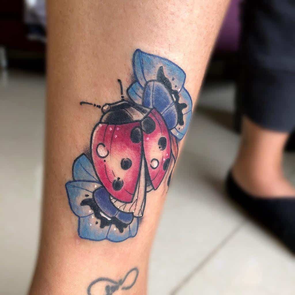 Neo-traditional ladybug tattoo with bold red wings, black dot details, and vibrant blue flowers, blending realism with artistic flair.