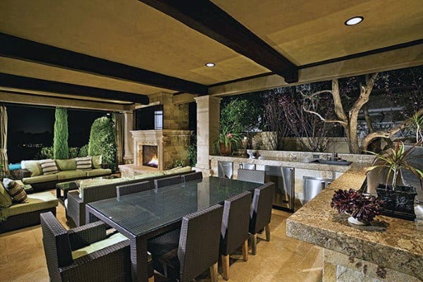 Luxurious outdoor patio with dining set, fireplace, kitchenette, and trees beautifully lit at night