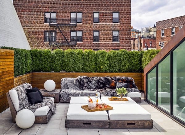 Urban rooftop patio with cushioned seating, greenery, and refreshments on a tray