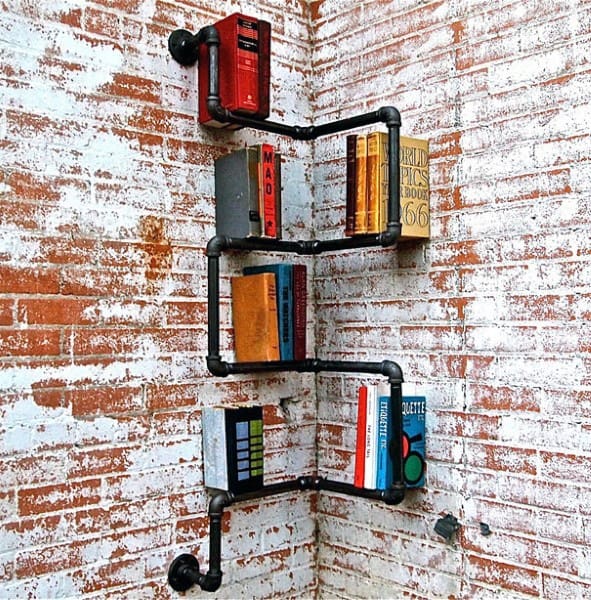 Industrial pipe bookshelf with books against a rustic brick wall