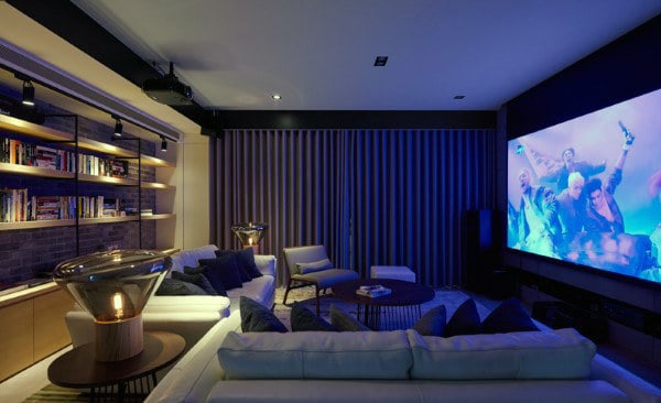 Home theater with a large screen, plush sofas, and atmospheric lighting; shelves with books are on the side wall
