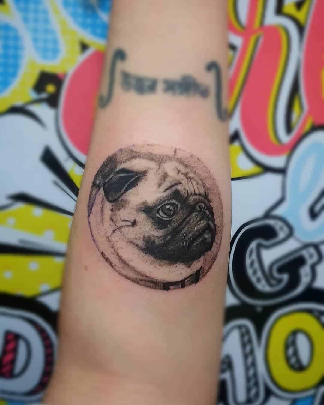 A realistic black-and-gray tattoo of a pug's face inside a circular frame, with detailed shading
