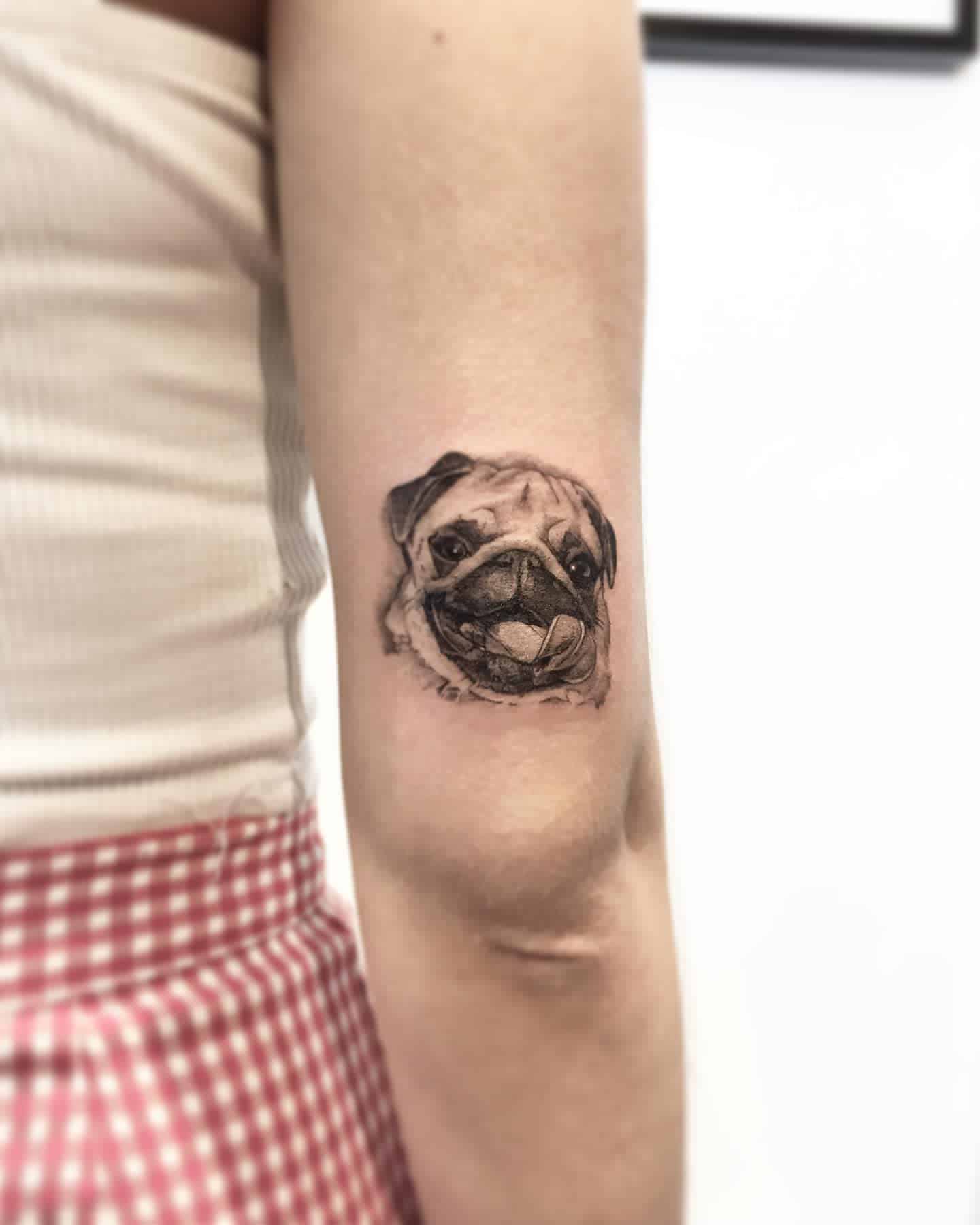 A realistic black-and-gray tattoo of a smiling pug, with fine detailing of its wrinkles and playful expression