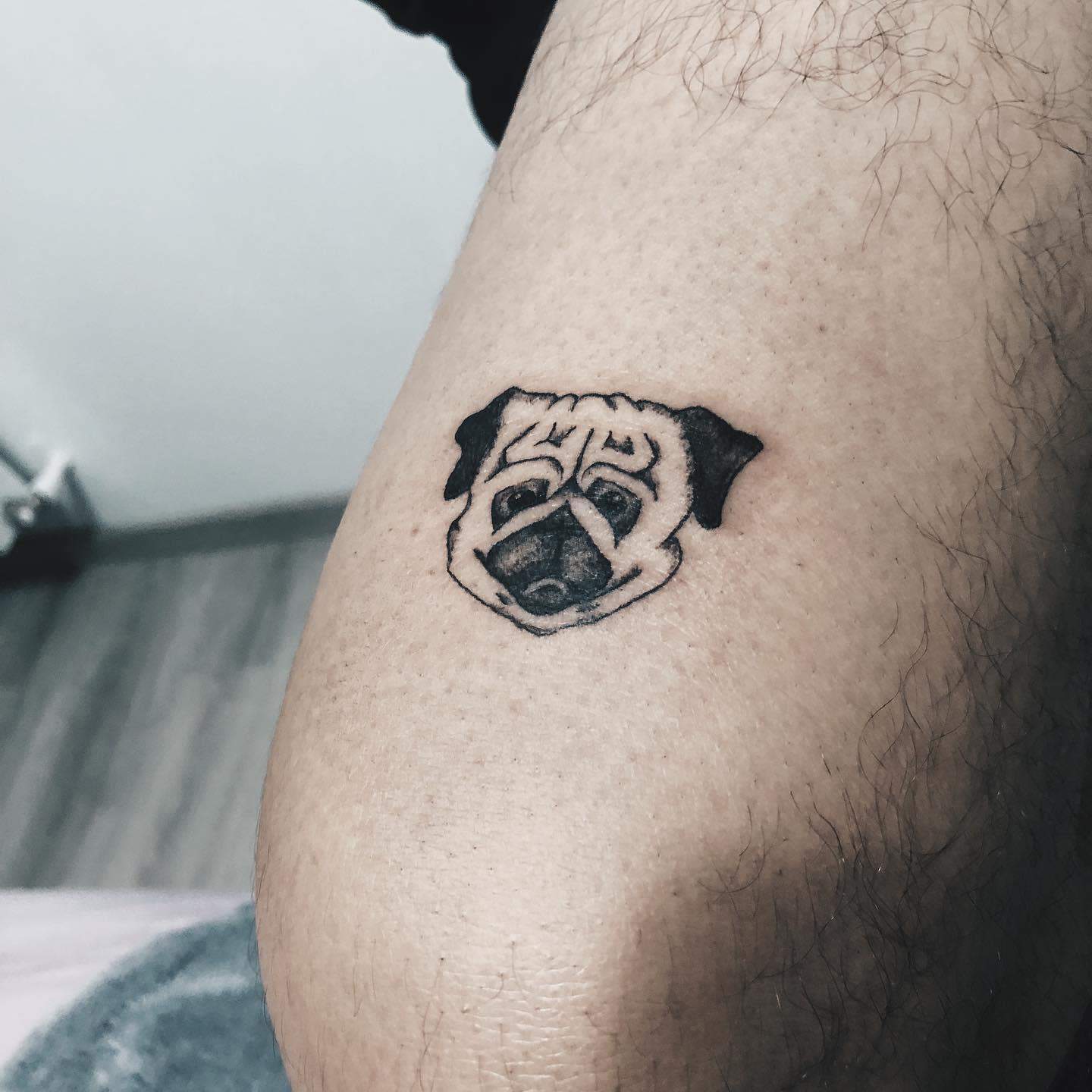 A small black-line tattoo of a pug's face, capturing its unique features with simple, clean lines and shading