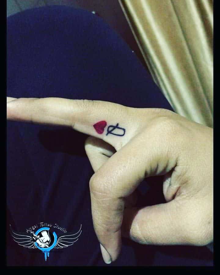 Minimal Queen of Hearts tattoo on the finger with a bold red heart and a simple black 'Q' for a stylish, discreet design