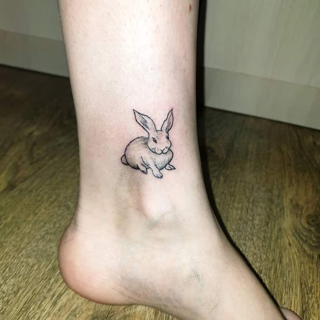 Minimalistic tattoo of a small bunny in a seated position, drawn with fine black lines