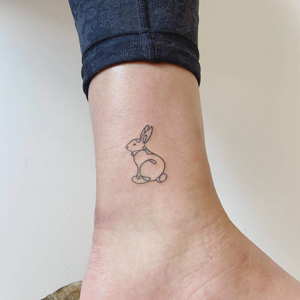 Simple line tattoo of a sitting rabbit, drawn with clean, minimalistic lines