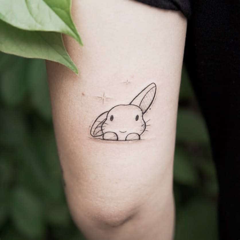 Delicate black line tattoo of a small bunny peeking out with a happy expression