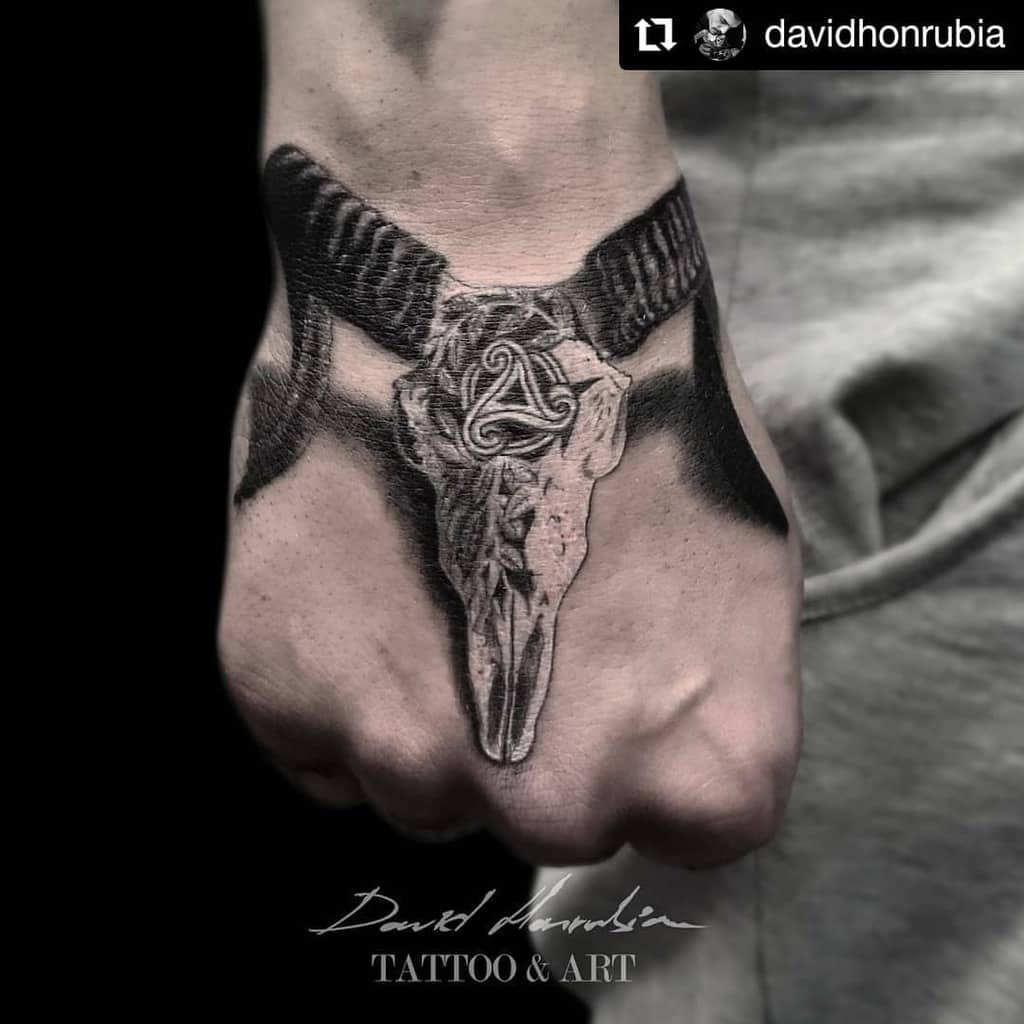 Hand tattoo featuring a ram skull with intricate horns and a Celtic knot on the forehead