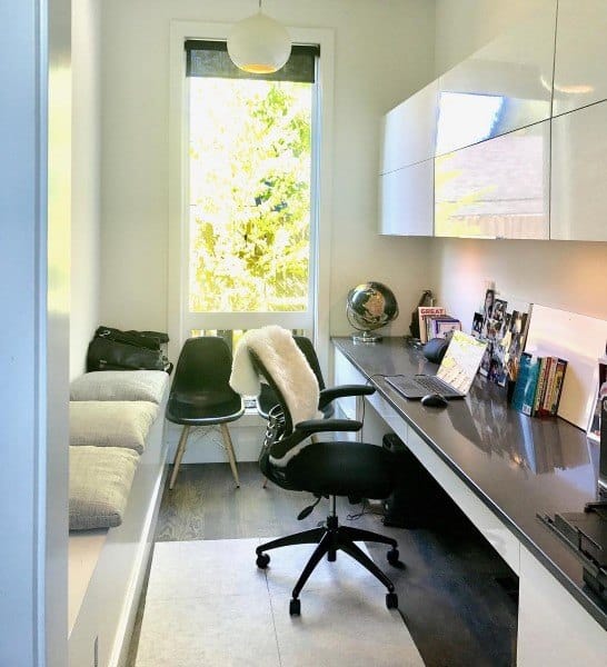 Bright home office with a built-in desk, globe, books, and a cushioned bench by a large window