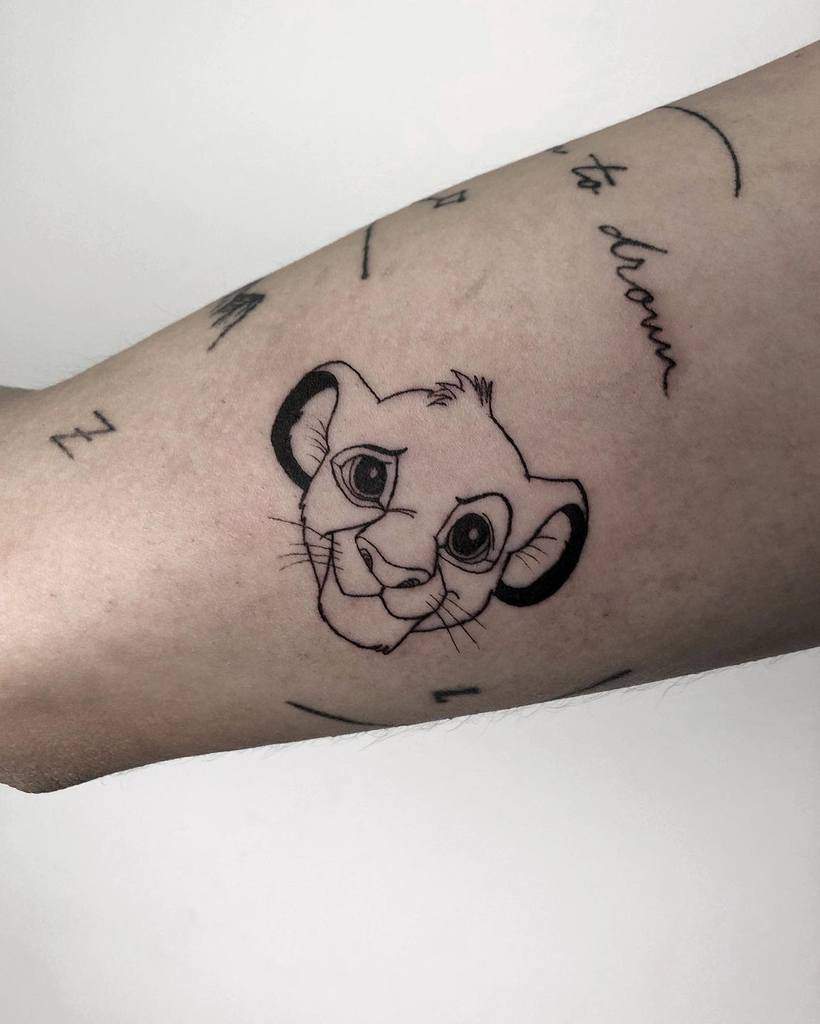 Simple black line tattoo of Simba’s face, highlighting his expressive eyes and playful smile
