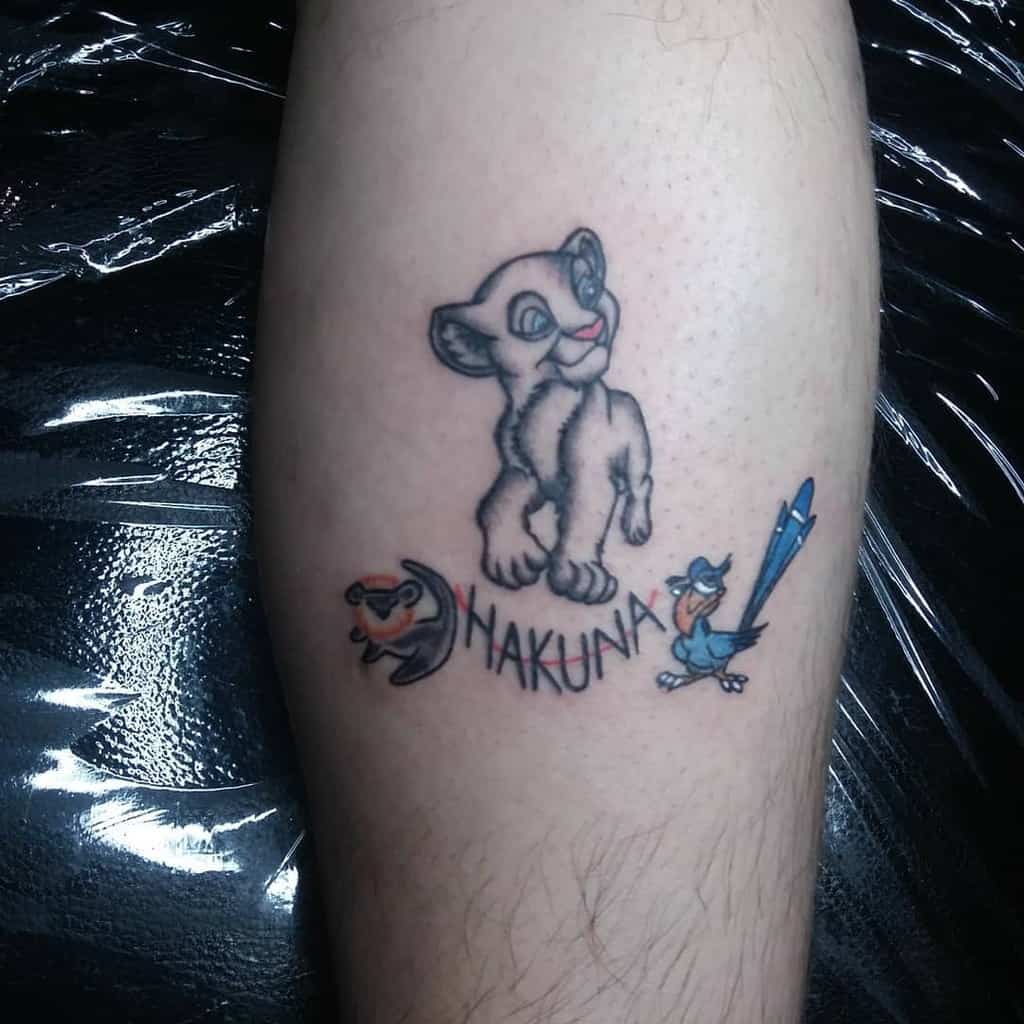 Vibrant tattoo featuring Simba in a playful pose with Zazu and Simba in his cute chibi version, accompanied by the 'Hakuna Matata' phrase in bold lettering